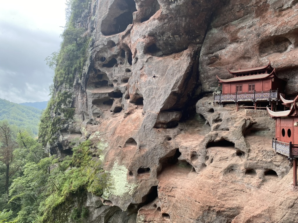 Ganlu Temple built into a Danxia cliff at Taining, Fujian — red sandstone walls overhanging the temple roofs