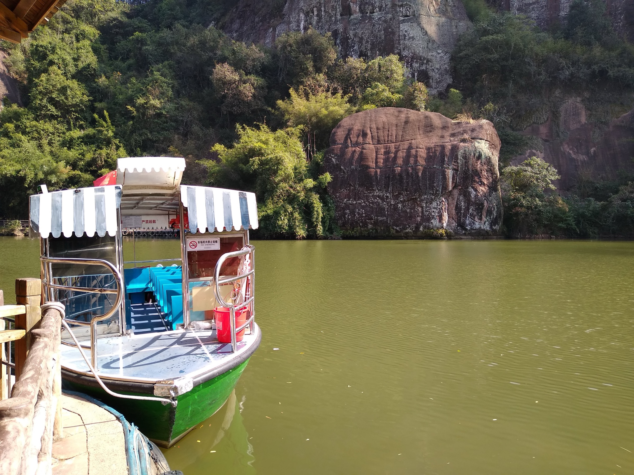 Boat docked at Chenglong Ting on Xianglong Lake, with the red Danxia cliffs rising directly from the water