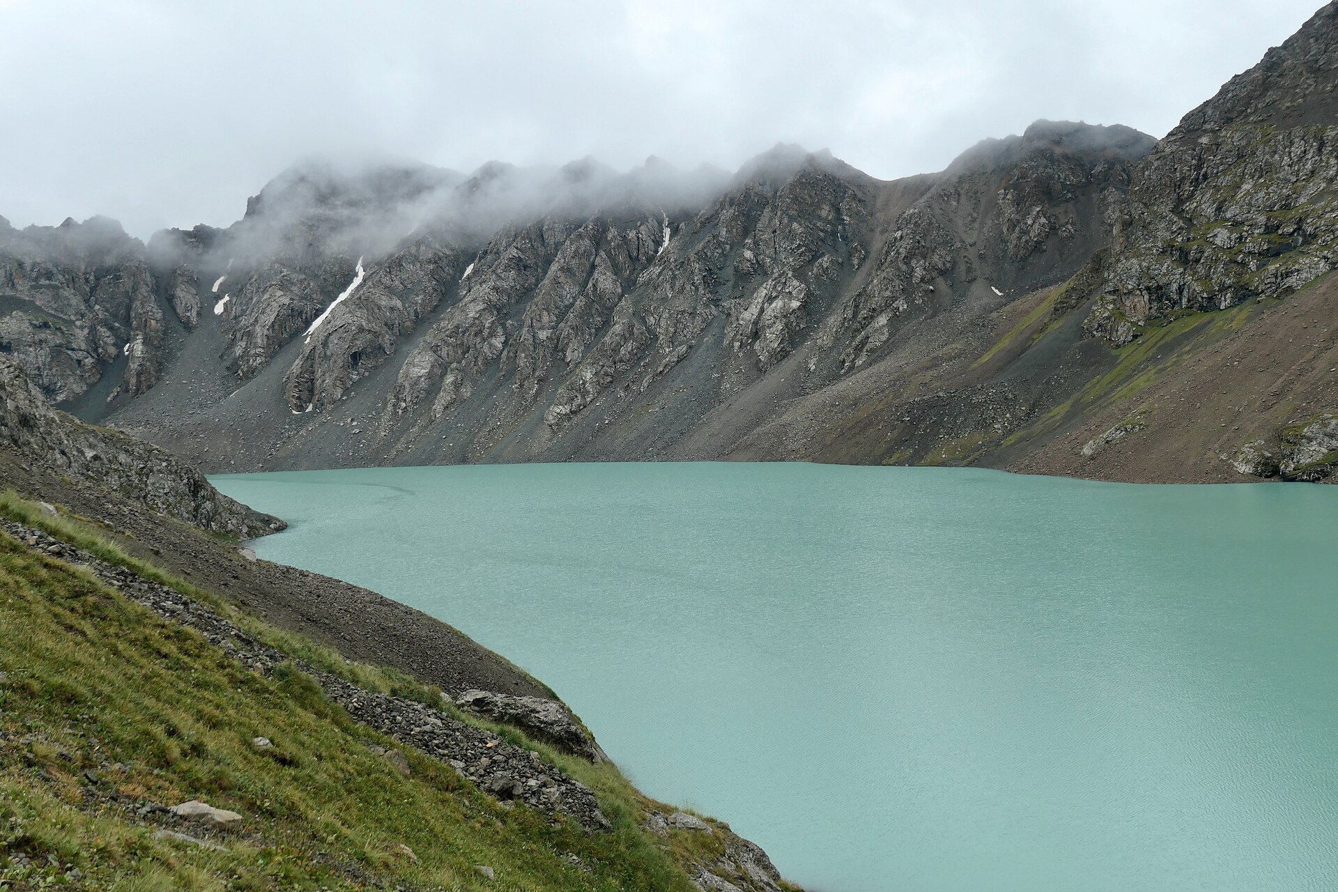 Ala-Kul beneath a dark rocky ridge and low cloud