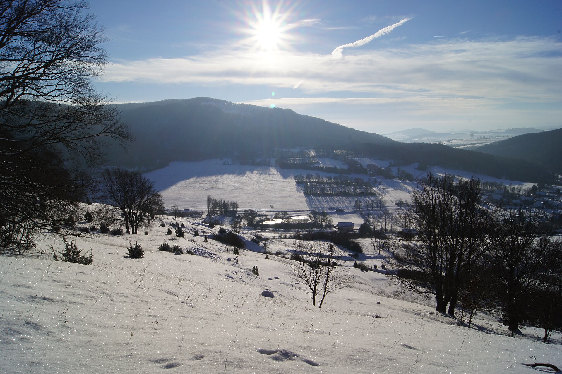 Sunlit snow covering the rolling hills and scattered woodland of the Rhön