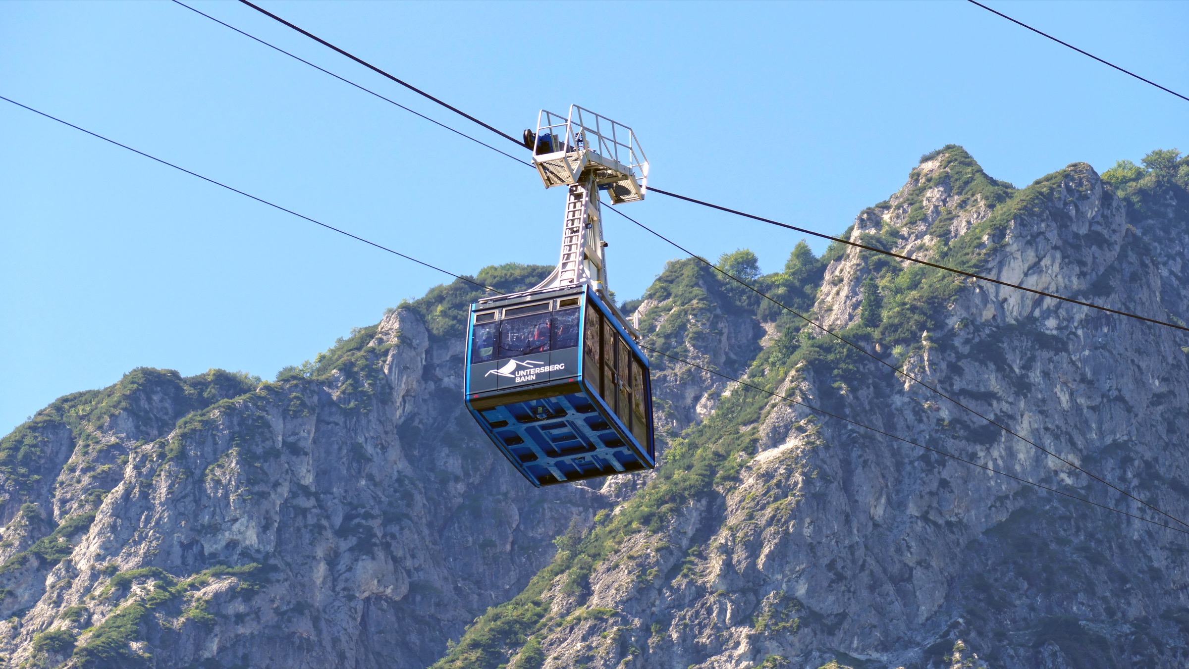 A red cabin of the Untersbergbahn cable car climbing above the wooded valley station south of Salzburg