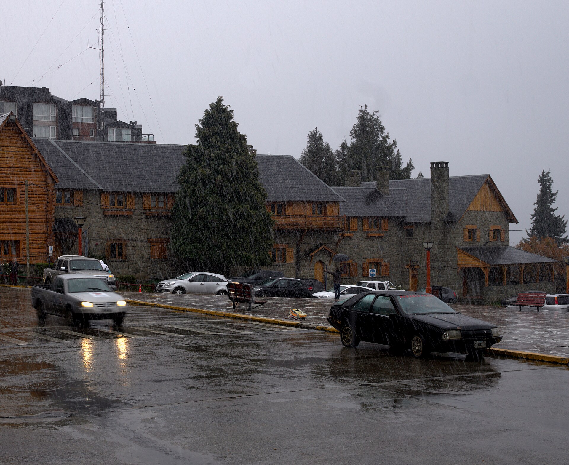 Cars passing the stone and timber buildings of Bariloche's Civic Centre in heavy precipitation