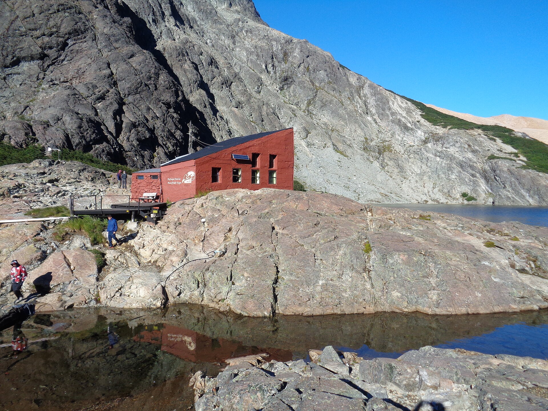 Red Refugio Italia beside dark Laguna Negra and steep rock walls