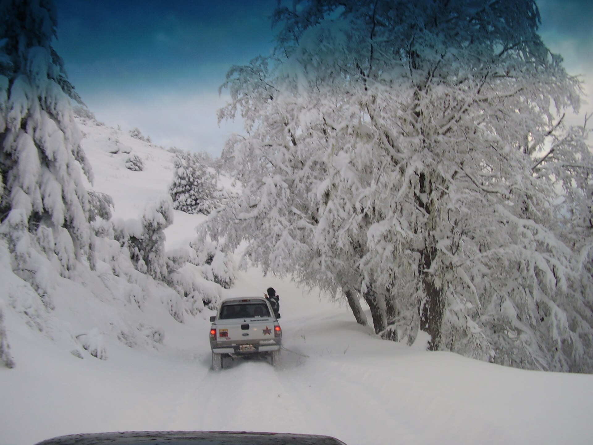 A vehicle following a narrow road through deep snow and white forest near Bariloche