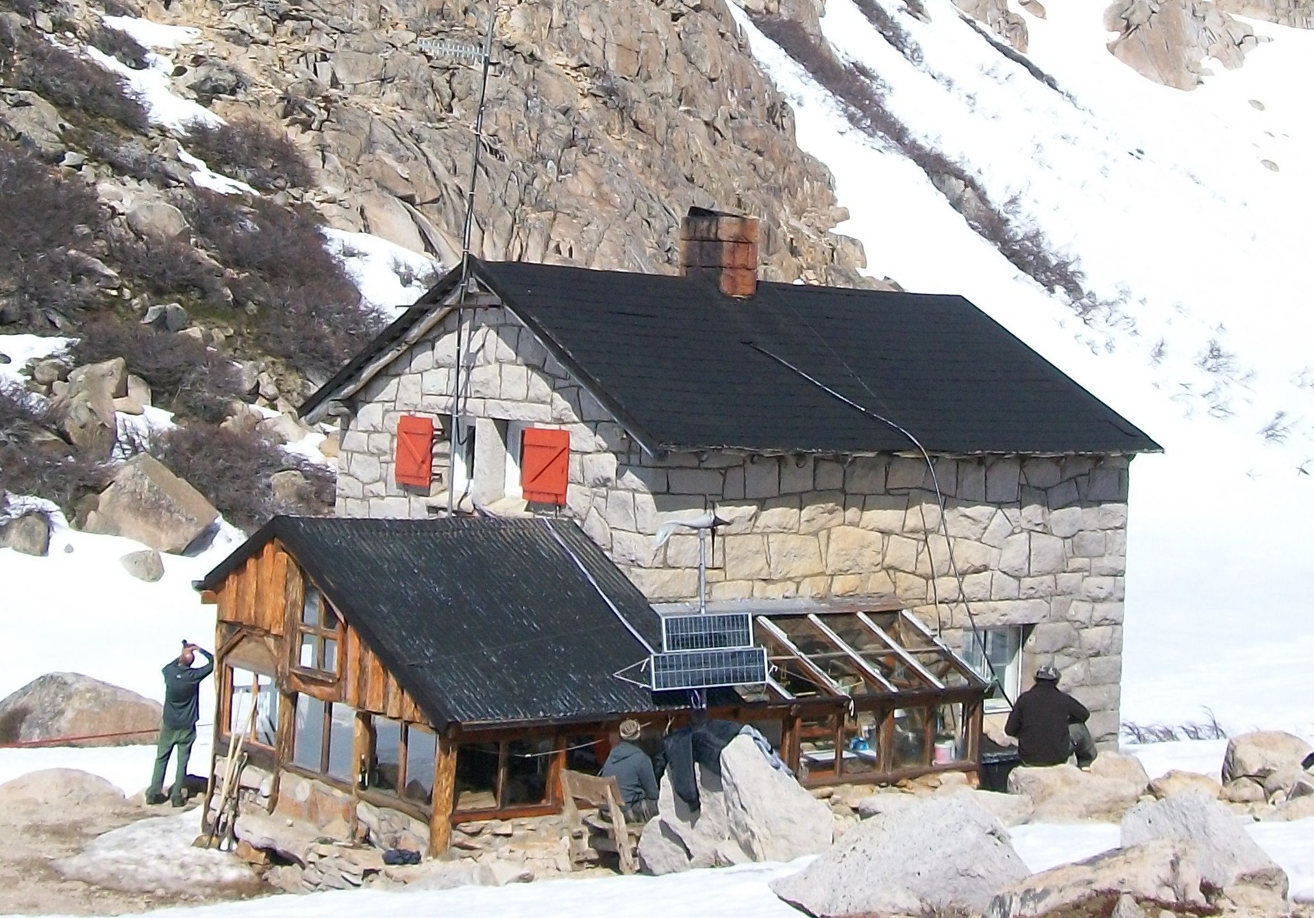 Stone Refugio Frey surrounded by snow beneath steep rock walls