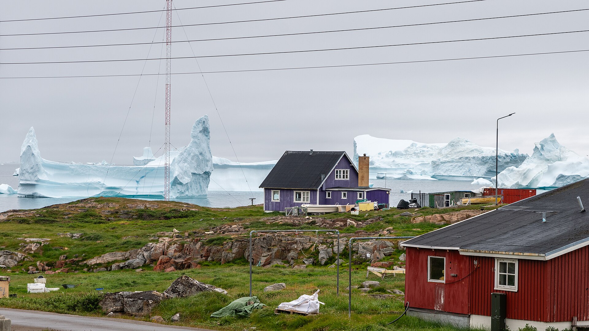 A house in Qeqertarsuaq with large icebergs drifting offshore in Disko Bay