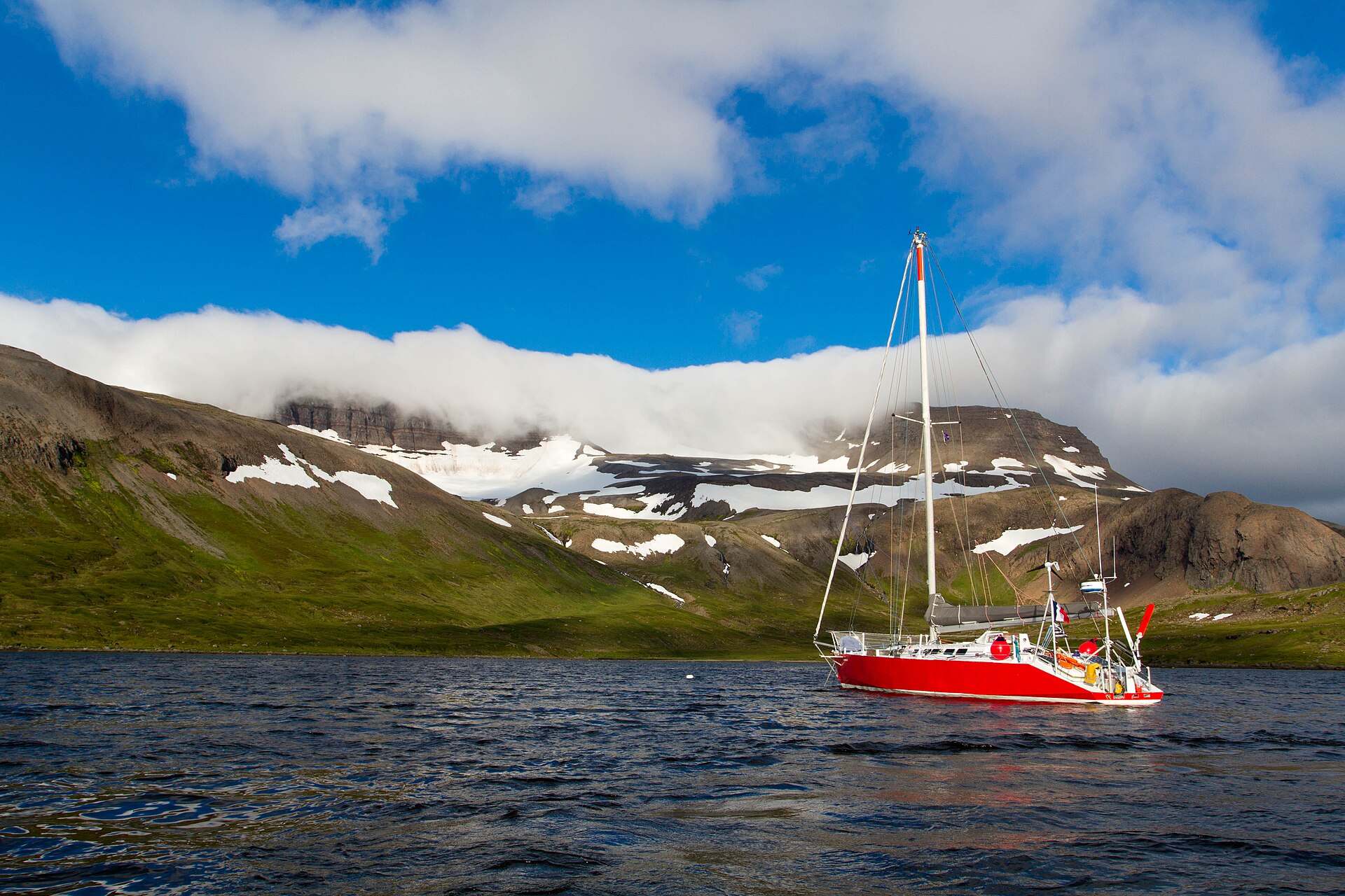 A red sailing yacht anchored beneath snow-streaked Westfjords mountains