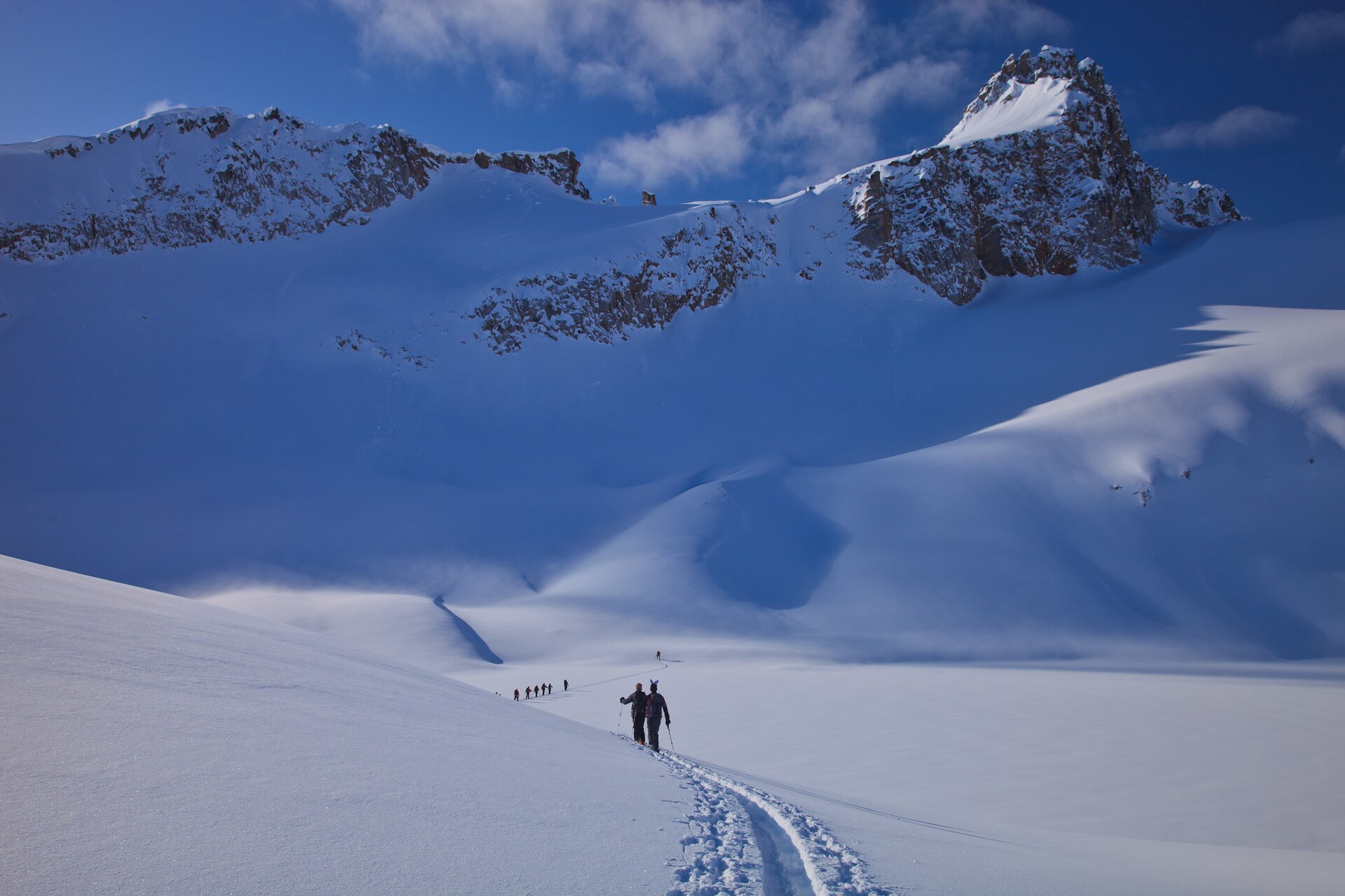 Ski tourers following an uptrack beneath snowy Selkirk peaks