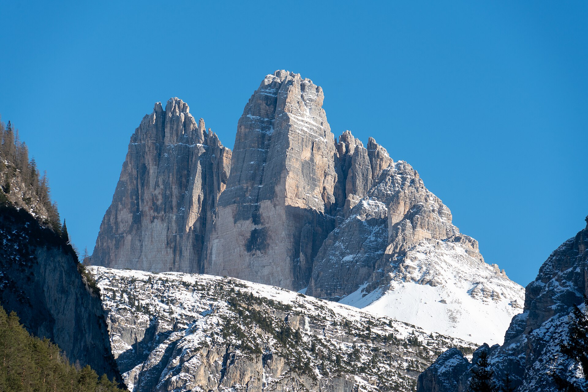 Tre Cime di Lavaredo rising above snow-covered slopes under a blue winter sky