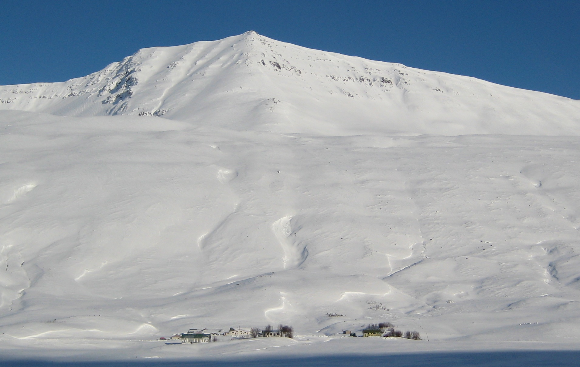 The deep snow-covered face of Syðrahvarf above farms in Skíðadalur