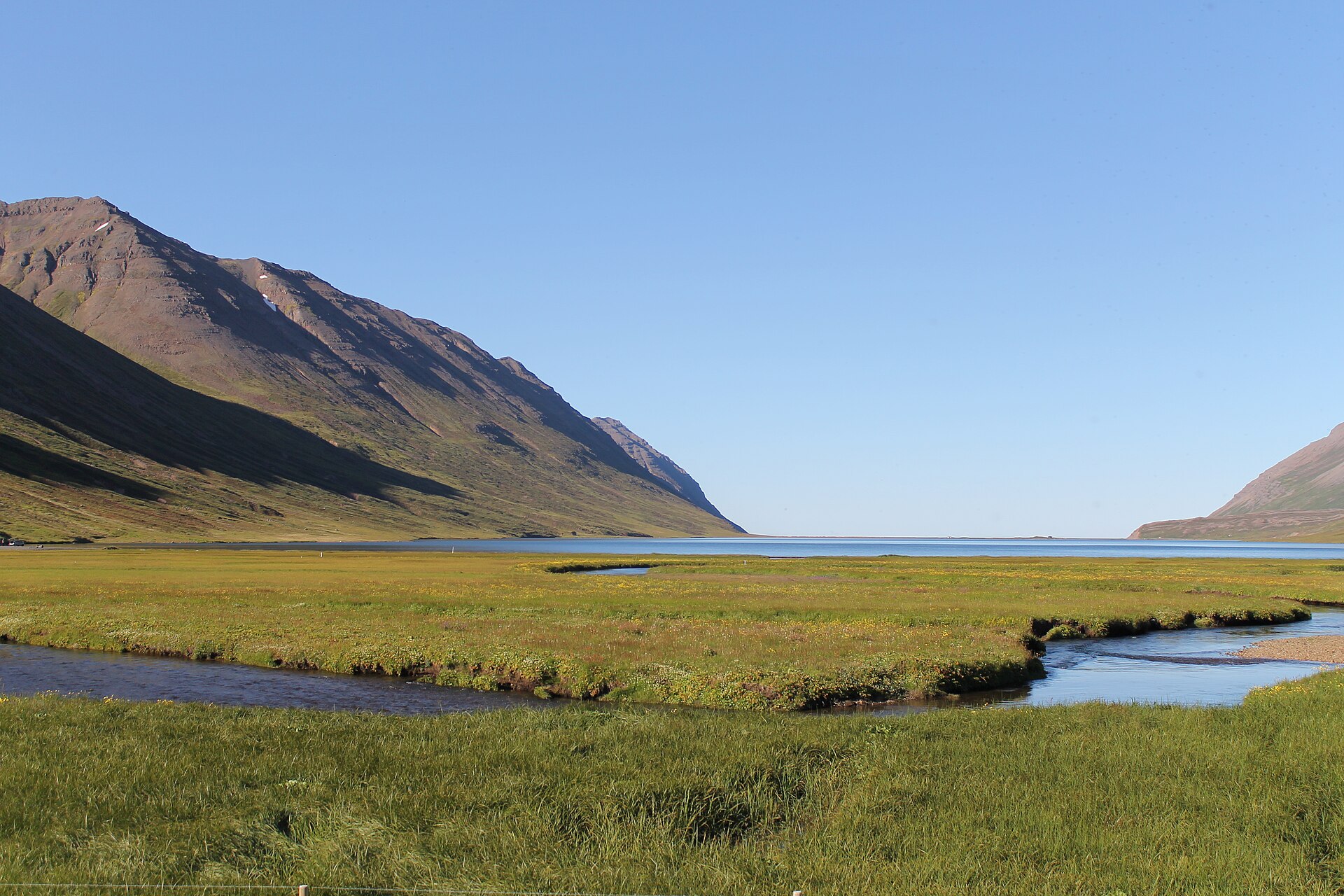 Hestfjall rising from the green shore of deserted Héðinsfjörður