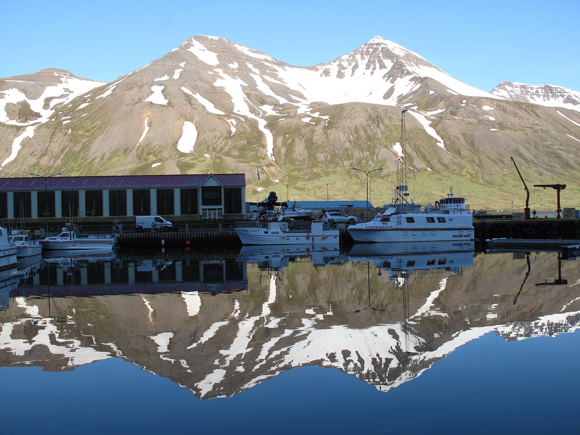 Snow-streaked mountains reflected in the still harbour at Siglufjörður