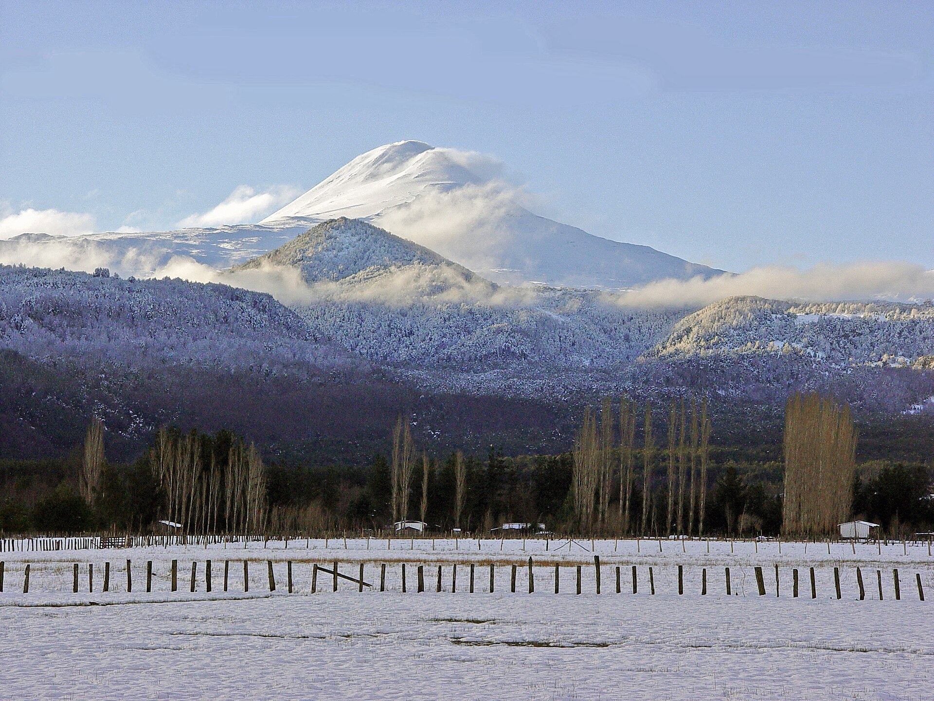 Snow-covered Llaima volcano rising beyond forest and fields